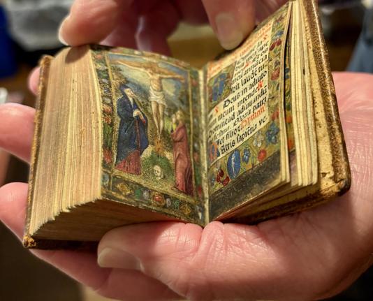 A little illuminated incunable book of hours in the palm of my hand, opened to a crucifixion scene.