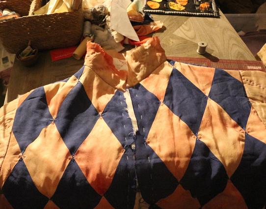 la veste posée sur une table. Le devant est alterné de losanges bleus et roses. il y a de petites broderies (des petits traits) au niveau des angles des losanges, mais on pourrait en mettre plus.