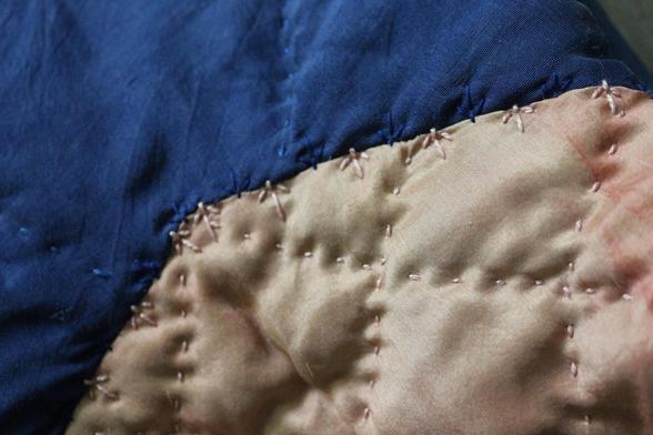 le bord du col, présentant la jonction entre le col rose et le tissu du dos, bleu. du côté rose, le bord du col est semé de petits points de broderie rose qui débordent un tout petit peu sur le bleu, et inversement. De loin les points sont presque invisibles.