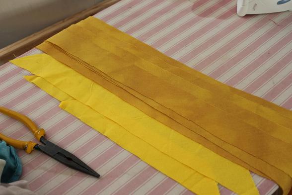 deux tas de biais, de longues bandes de tissu fine, jaune. à gauche le biais est d'un jaune vif uniforme ; à droite après teinture le jaune est plus doré, plus sombre, et la teinture n'est pas uniforme, laissant des zones plus ou moins claires.