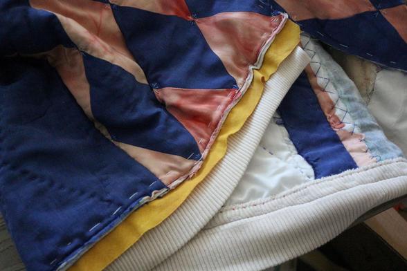 on voit, superposées et cousues à 5 millimètre du bord, les quatre épaisseurs qui forment le blouson : le tissu extérieur rose et bleu, la ouate, le biais jaune pas encore rabattu, le bord côte beige.