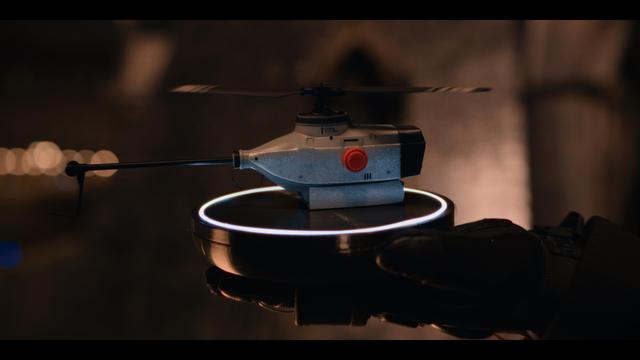 A CG drone hovering above a circular platform with a glowing blue ring, held by a gloved hand. The text reads: "AIR FORCE AUCTION".