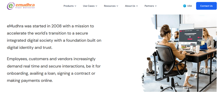 Screenshot of eMudhra's website. Text: "eMudhra was started in 2008 with a mission to accelerate the world's transition to a secure integrated digital society with a foundation built on digital identity and trust. Employees, customers and vendors increasingly demand real time and secure interactions, be it for onboarding, availing a loan, signing a contract or making payments online." Picture: stock photograph of an office lady typing on a computer.