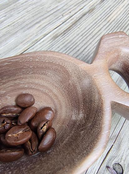 détail en gros plan d'une cuillère en bois foncé avec un manche court et percé d'un trou, en forme de queue de poisson, remplie de grains de café