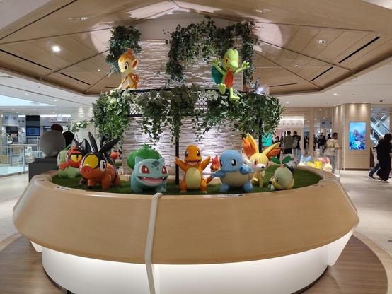 Photo d'une grosse colonne d'un immeuble décorée de plein de pokémon tout autour et de fausses plantes vertes.