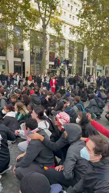 Des manifestant⋅e⋅s assis⋅e⋅s puis se lèvent et chantent lors de la manifestation du  17 octobre.