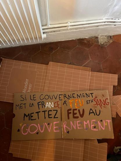 Pancarte au sol sur carton : "si le gouvernement met la france à feu et à sang mettez feu au gouvernement"