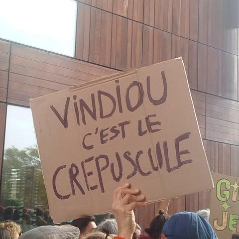 Pancarte tenue par quelqu'un dans une foule. 
Texte dessus :" Vindiou c'est le crépuscule"