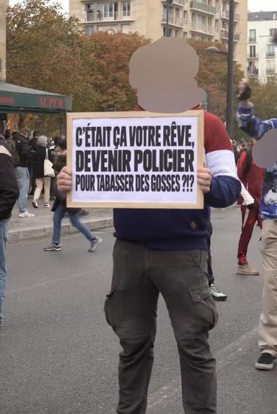 Une personne tenant un panneau qui indique « Était-ce votre rêve de devenir policier pour frapper des enfants ?! » dans une rue lors d'une manifestation.