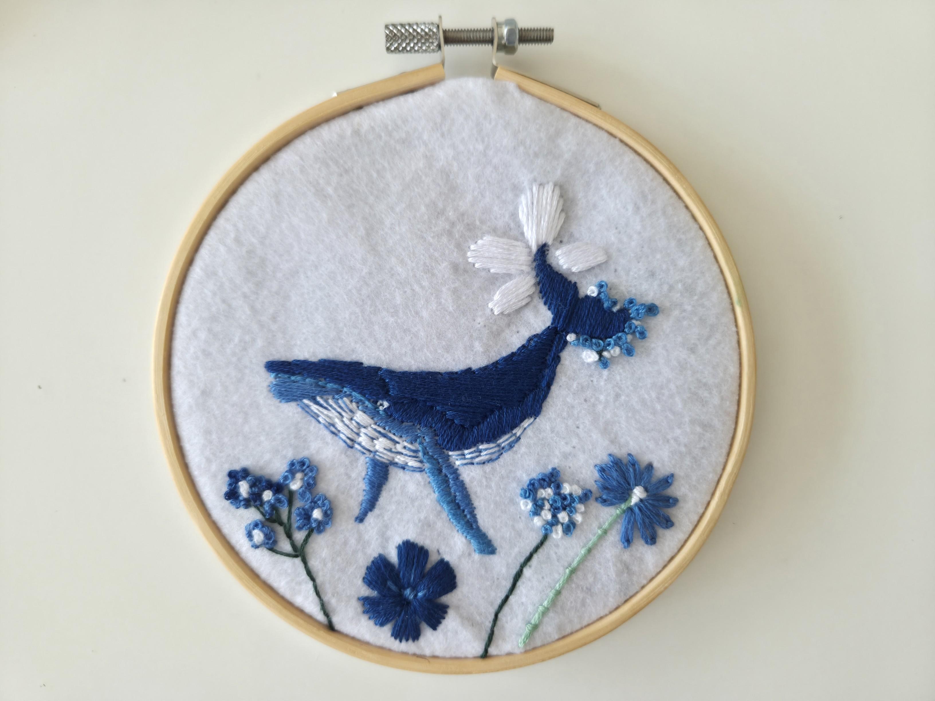 La broderie représente une baleine et des fleurs dans des nuances de bleu et blanc.
́Elle est dans un cercle en bois de 15 cm.