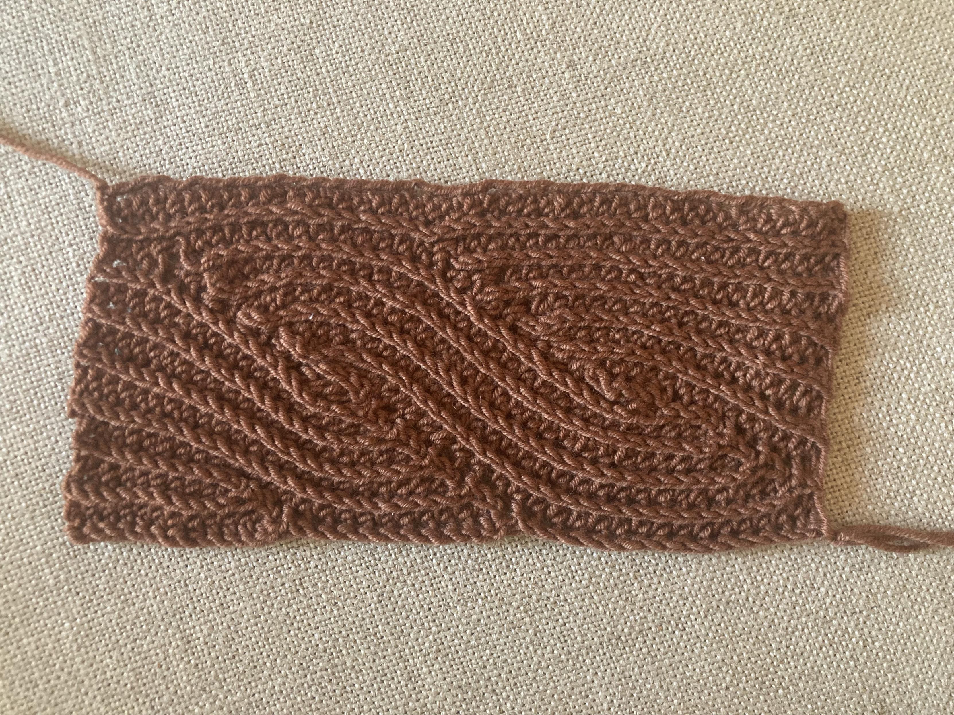 Échantillon au crochet rectangulaire, le fil est assez fin, couleur noisette (ourson selon la marque) et les points de crochet forment un motif torsadé, un peu comme des vagues.
