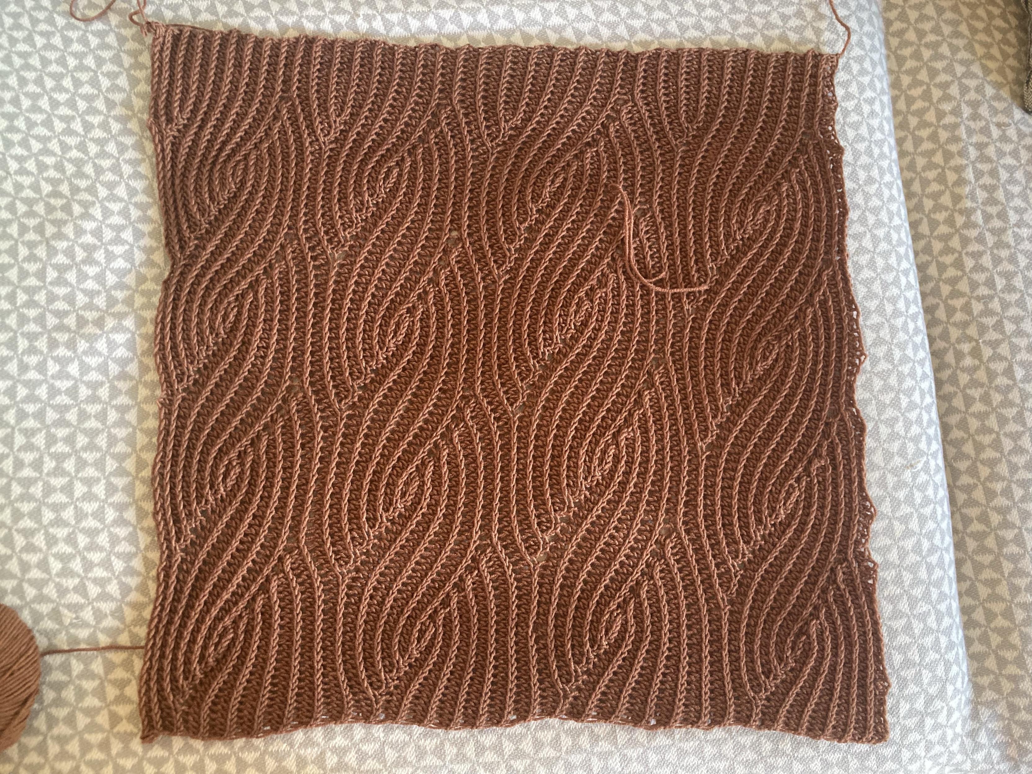 Carré de tissu crocheté, le fil est assez fin, couleur noisette (ourson selon la marque) et les points de crochet forment un motif torsadé, un peu comme des vagues.